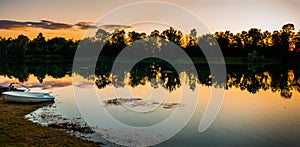 Beautiful Golden Sunset over the lake with forest reflection and a lonely boat