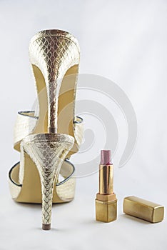 Beautiful golden women`s sandals and open red lipstick on white background.