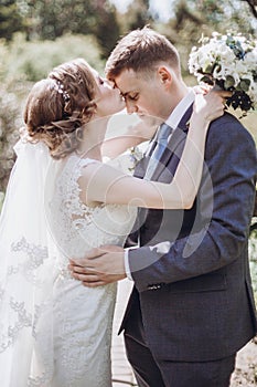 Beautiful gorgeous bride and groom kissing in sunny spring park and enjoying day. happy wedding couple relaxing in green garden.