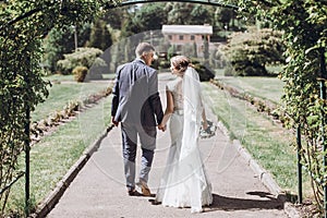 Beautiful gorgeous bride and groom posing in sunny spring park among green leaves. happy wedding couple walking in green garden. photo