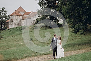 Beautiful gorgeous bride and groom walking outdoors. happy wedding couple hugging and embracing at old castle. happy romantic