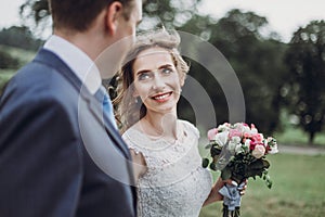 Beautiful gorgeous bride and groom walking in sunny park and embracing. happy wedding couple looking at each other in green garden