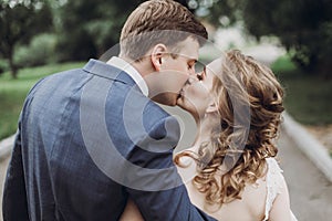 Beautiful gorgeous bride and groom walking in sunny park and kissing. happy wedding couple hugging in green garden at old castle.