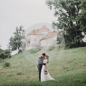 Beautiful gorgeous bride and groom walking in sunny park and kissing. happy wedding couple hugging in green garden at old castle.