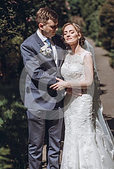 Beautiful gorgeous bride and groom walking in sunny spring park and enjoying day. happy wedding couple relaxing in green garden.