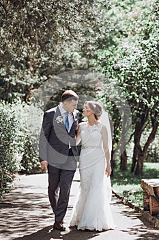 Beautiful gorgeous bride and groom walking in sunny spring park and enjoying day. happy wedding couple relaxing in green garden.