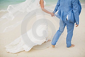 Beautiful gorgeous bride and stylish groom holding hands, on the background of a sea.