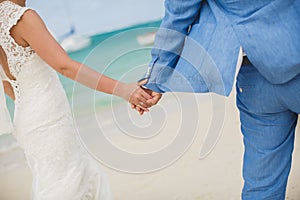 Beautiful gorgeous bride and stylish groom holding hands, on the background of a sea.