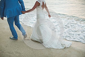 Beautiful gorgeous bride and stylish groom holding hands, on the background of a sea.