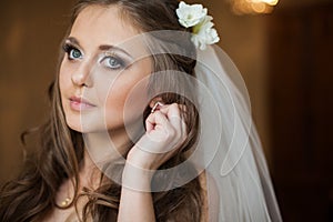Beautiful gorgeous brunette bride putting on luxury earrings in
