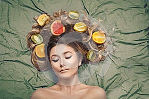 Beautiful gorgeous model girl with colorful citrus healthy fruits in her shiny hair. Care and hair products. Hair care concept. Ha