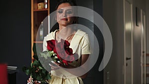 Beautiful and gorgeous woman in bathrobe smelling bouquet of red roses.