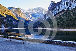 Beautiful Gosausee lake landscape with a bench, forest, clouds and reflections in the water in Austrian Alps.