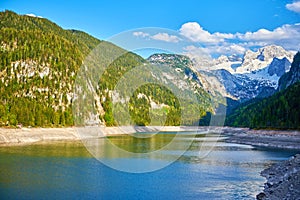 Beautiful Gosausee lake landscape with Dachstein mountains, forest, clouds and reflections in the water in Austrian Alps