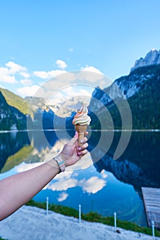 Beautiful Gosausee lake landscape with hand and ice cream, Dachstein mountains, forest, clouds and reflections in the water in Aus