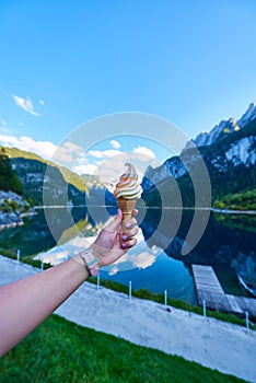 Beautiful Gosausee lake landscape with hand and ice cream, Dachstein mountains, forest, clouds and reflections in the water in Aus