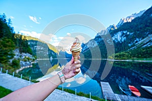 Beautiful Gosausee lake landscape with hand and ice cream, Dachstein mountains, forest, clouds and reflections in the water in Aus