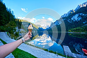 Beautiful Gosausee lake landscape with hand and ice cream, Dachstein mountains, forest, clouds and reflections in the water in Aus