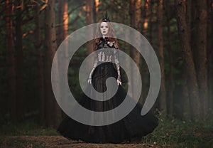 A beautiful gothic princess with pale skin and very long red hair in a black crown and a black long dress in a misty fairy forest.