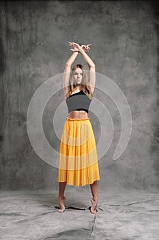 A beautiful graceful slender female dancer performs choreographic figures and movements on a gray dark fabric background