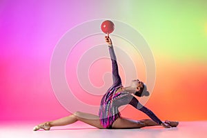 Beautiful, graceful sport. Young sportive girl, rhythmic gymnast in twine with red ball isolated on colored neon photo