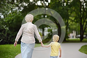 Beautiful granny and her little grandson walking together in park