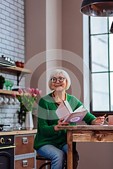 Beautiful granny smiling to someone calling while keeping a book