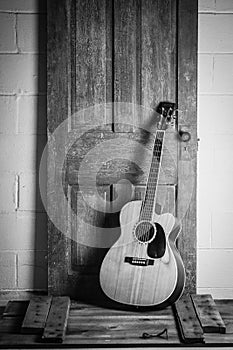 Beautiful grayscale shot of an acoustic guitar leaned on a wooden door on a wooden surface