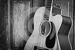 Beautiful grayscale shot of an acoustic guitar leaned on a wooden door on a wooden surface