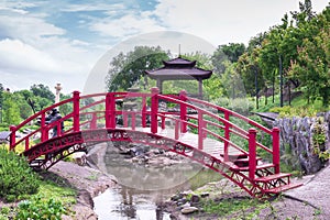 Beautiful green botanical landscape design in garden, city park with red wooden bridge through decorative lake pond