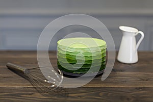 Beautiful green cake stands on dark wooden board, close corolla and white pitcher