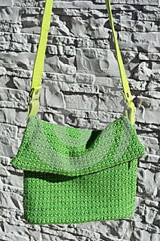 Beautiful green crocheted handbag with green handle behind the gray stone wall in the garden in summer