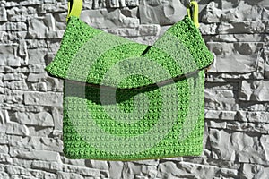 Beautiful green crocheted handbag with green handle behind the gray stone wall in the garden in summer