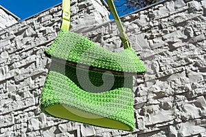 Beautiful green crocheted handbag with green handle behind the gray stone wall in the garden in summer