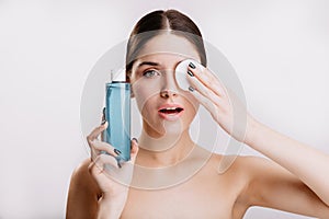 Beautiful green-eyed girl put cosmetic sponge on her face, removing dirt. Portrait of healthy woman without makeup on