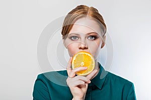 Beautiful green eyed, redhead woman covers her lips with a slice of orange. Well groomed skin, clean face with makeup,