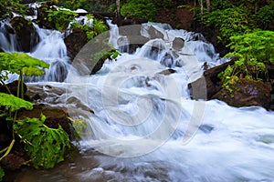 In the beautiful green forest on the huge rocks the fast tempestuous mountain waterfall flows. photo