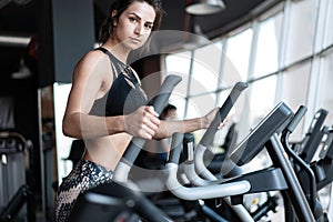 Beautiful gym woman exercising on a cardio machine smiling.