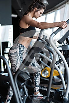 Beautiful gym woman exercising on a cardio machine smiling.