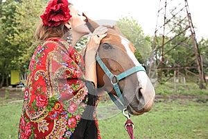 Beautiful gypsy girl in bright clothes with a horse on a farm