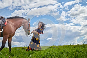 Beautiful gypsy girl leads a stubborn, unruly horse in field with green glass in summer day and blue sky and white clouds