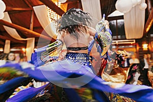 Beautiful gypsy girls dancing in traditional blue floral dress at wedding reception in restaurant. Woman performing romany dance