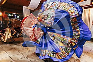 Beautiful gypsy girls dancing in traditional blue floral dress at wedding reception in restaurant. Woman performing romany dance