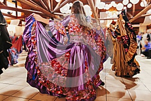 Beautiful gypsy girls dancing in traditional purple floral dress at wedding reception in restaurant. Woman performing romany dance