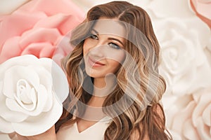 Beautiful hair. Woman beauty portrait smiling with makeup and long healthy hairstyle over pink white roses flowers