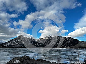 Beautiful half-frozen lake and mountains against the background of the cloudy blue sky. Canada.