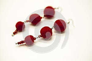 Beautiful hand-made earrings felted wool sheep red shades on a white background, close-up.