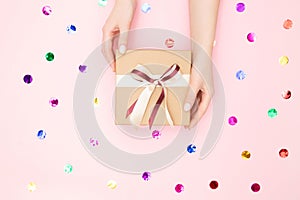 Beautiful hands girl hold gift box present craft paper on pink background, top view. Concept Christmas, New Year