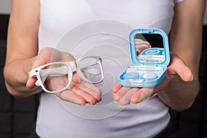 Beautiful hands hold soft contact lenses and a container for them, and glasses