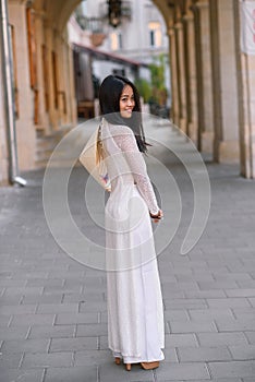 Beautiful happy asian girl dressed in Ao Dai dress with vietnamese conical hat against arches background.